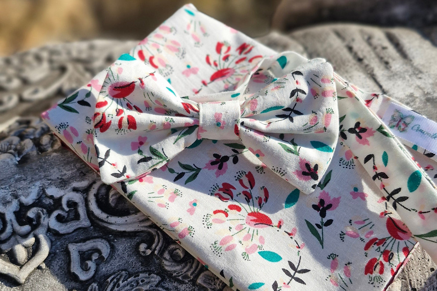 ensemble composé d'un nœud papillon et de sa pochette fleurie assortie. fleurs éparses tons rouges sur fond blanc