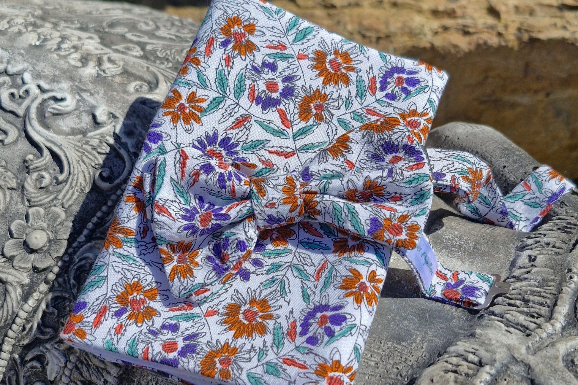 ensemble noeud papillon et pochette de costume assortis, cousu dans un tissu de récupération dont la composition exacte est inconnue. Motifs fleurs abstraites de couleurs oranges, parme et feuillages verts sauge